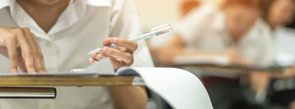 School student\'s taking educational exam, thinking hard, writing answer with left hand in classroom for education, university admission test  and world literacy day concept