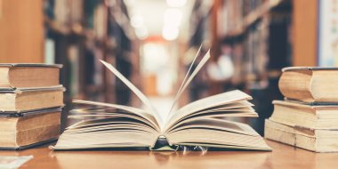 Eski açık ders kitabıyla kütüphanede kitap, okuma masasında edebiyat metin arşivi yığını ve akademik eğitim öğrenme kavramı için okul çalışma odası arka planındaki kitaplıklar.