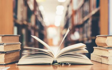 Eğitim öğrenme kavramı, eski kütüphanede kitap veya ders kitabı açmak, edebiyat metni yığınlarını okuma masasına yığmak, ve okul çalışma odası arka planında kitaplıkların koridoru 