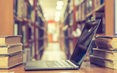 Bulanık okul kütüphanesinde bilgisayar defteri açık olan eğitim e-öğrenme sınıfı ve e-kitap dijital teknoloji kavramı veya eski kitap yığınları, ders kitabı arşivi koleksiyonu arasında sınıf arkaplanı