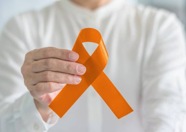Orange ribbon for awareness on Leukemia, Kidney cancer, RDS disease, multiple sclerosis, ADHD illness, Chronic Obstructive Pulmonary Disease (COPD) in person's hand clipart