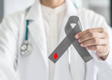 Diyabet Bilinci Dünya Diyabet Günü kurdelesi. Doktorun elinde diyabetik hastalığı olan hastayı desteklediği için gri yay üzerine kırmızı kan damlası.