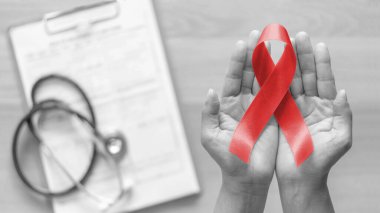 World aids day and national HIV/AIDS and ageing awareness month with red ribbon on woman hand support (bow isolated with clipping path) clipart