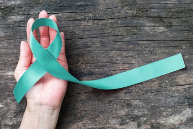 Teal ribbon awareness on woman's hand for Ovarian Cancer, Polycystic Ovary Syndrome (PCOS) disease, Post Traumatic Stress Disorder (PTSD), Tourette's Syndrome, Obsessive Compulsive Disorder (OCD) clipart