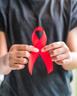 Genç kızların Dünya Yardım Günü ve HIV / AIDS farkındalık ayı kampanyası için el desteğine kırmızı kurdele takıyor