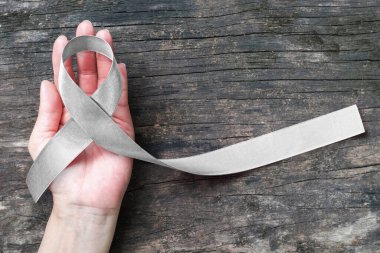 Silver color ribbon on hand support and ols aged wood (isolated with clipping path) for Parkinson's disease awareness and Brain cancer tumor illness clipart