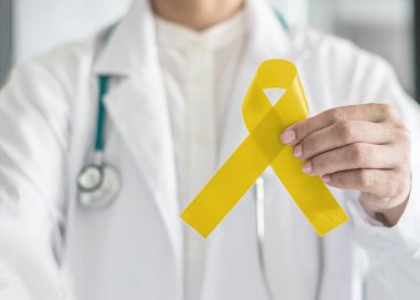 Sarkoma kanseri farkındalığı için sarı kurdele sembolik renk ve doktorun elinde intihar önleme