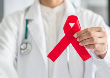 Dünya AIDS ve HIV virüsü farkındalığı konsepti için doktor elinde kırmızı kurdeleye yardımcı olur 