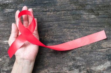 Kırmızı kurdele farkındalığı (kırpma yolu) insan eli, ağaç zemin üzerinde: HIV hastalığıyla yaşayan insanlara destek olmak için dünya yardımları günü kampanyası