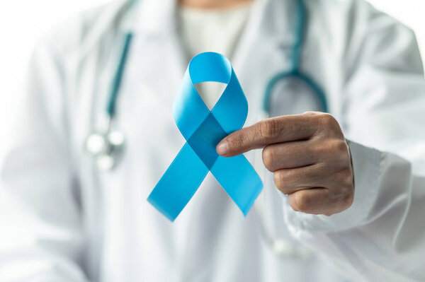 Prostate cancer blue awareness ribbon for men health in November with light blue bow color on medical doctor's hand in clinical lab gown in hospital, male patient healthcare concept