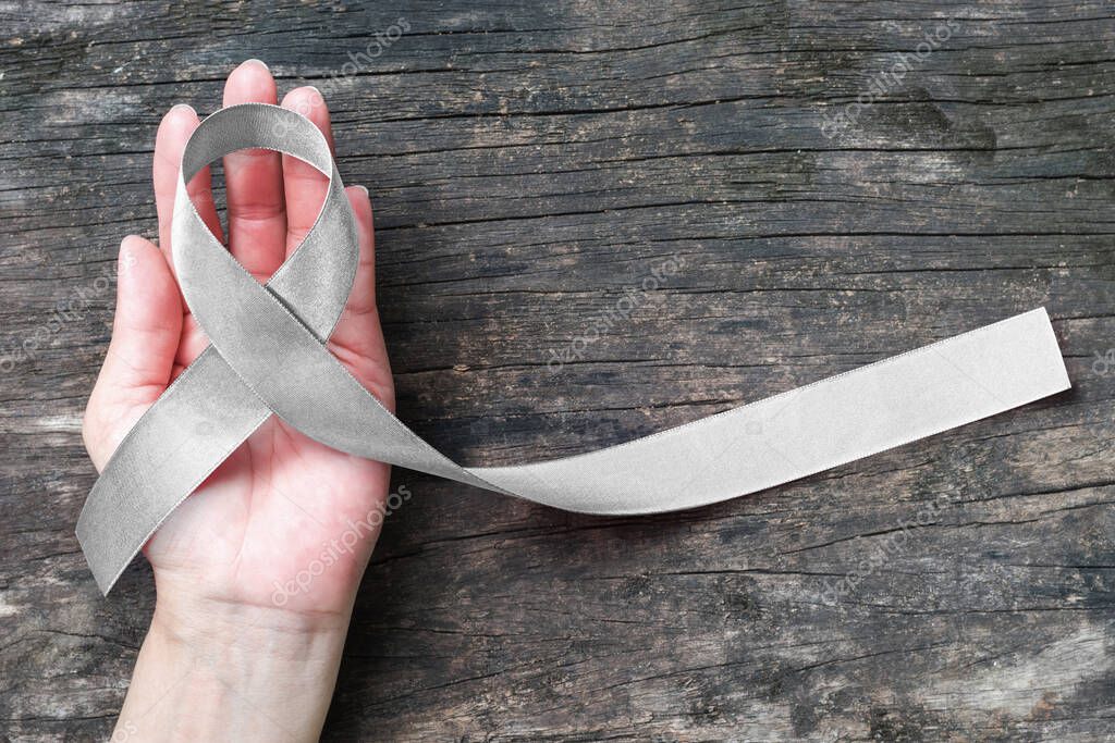 Silver color ribbon on hand support and ols aged wood (isolated with clipping path) for Parkinson's disease awareness and Brain cancer tumor illness