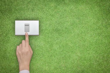 Enerji tasarrufu ve çevre dostu kavram. Yeşil çimlerin üzerindeki el kapatma düğmesi. 