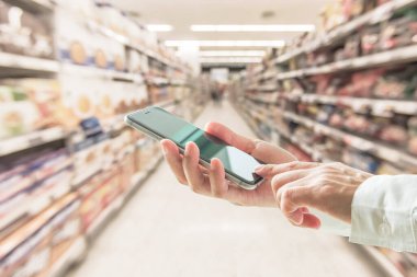 Süpermarkette perakende alışveriş yapmak için cep telefonu kullanan dijital iş adamı ya da alışverişçi 