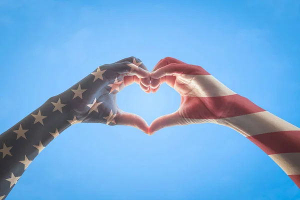 United States of America -USA American flag pattern on people hands in heart love shape isolated on blue sky background