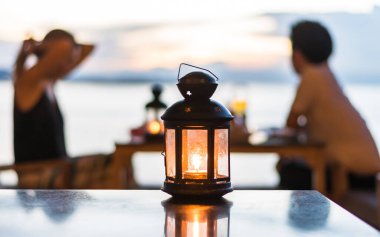 Romantik çift, sevgililer günü için restoran kafeteryasında altın saat boyunca mum ışığı feneri ve alacakaranlık bulutları altında arka planda akşam yemeği bulanıklığı yaşıyor.