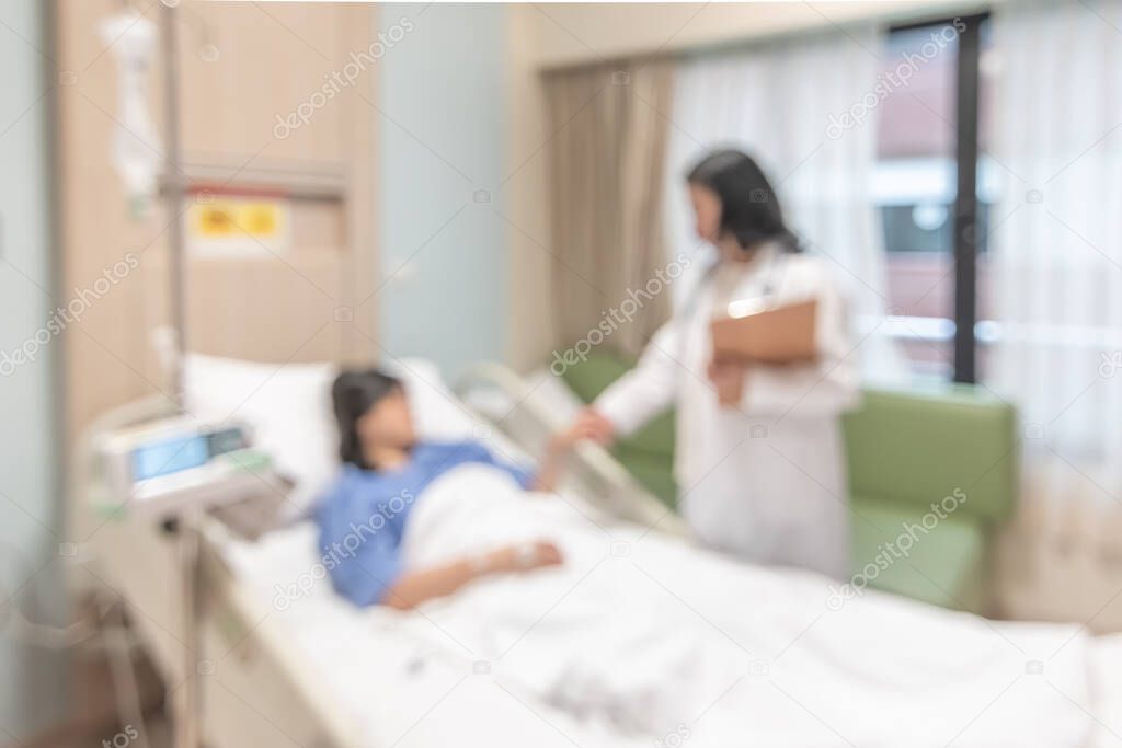 Doctor visiting patient on hospital bed, medical blurred background with blurry interior white room ward with nursing care or healthcare recovery treatment