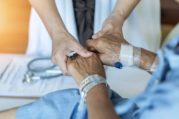 Yatakta yaşlı yaşlı bir hasta, yaşlı bir doktorla birlikte güven ve hemşirelik için el ele tutuşuyor, tıbbi tedavi, bakıcı ve hastane sağlık servisinde yatılı hasta 