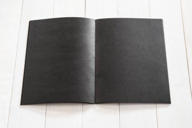 Boş A4 boyutundaki siyah kitap şablonu, kremsi beyaz yüzey ahşap masa üzerine yerleştirilmiş açık çift sayfa ile taklit