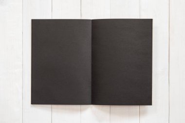 Boş A4 boyutundaki siyah kitap şablonu, kremsi beyaz yüzey ahşap masa üzerine yerleştirilmiş açık çift sayfa ile taklit