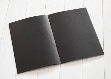 Boş A4 boyutundaki siyah kitap şablonu, kremsi beyaz ahşap masaya yerleştirilmiş çift sayfalı bir şablon oluşturur.