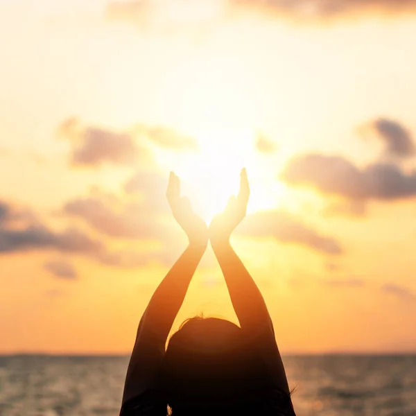 Yaz güneşi, Haziran gündönümü kavramı ve mutlu genç kadın ellerinin silüeti dinleniyor, meditasyon yapıyor ve gün batımını tutuyor okyanus ya da deniz arka planında sıcak altın saat gökyüzüne karşı..