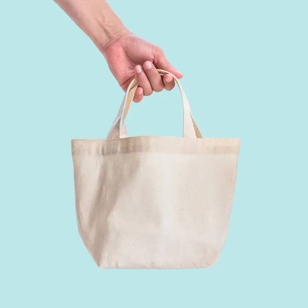 袋口帆布白色棉布用于生态肩购物袋模型空白模板 蓝色背景 裁剪路径 与妇女的手操作手柄带子隔离 — 图库照片
