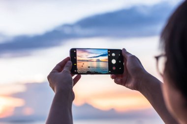 PATTAYA, THAILAND-22 Ocak 2018: Zirvedeki S8 Smartphone kamerası, gün batımında altın mutlu saat şafağında bulutlarla güzel deniz manzaralı gökyüzünün dokunuşuyla fotoğraf çeken kadının ellerinde 