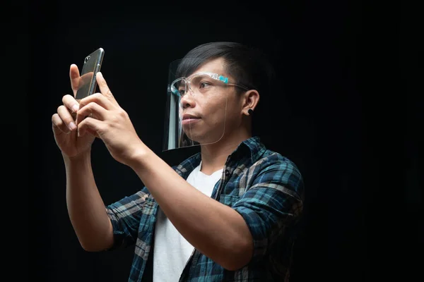Man wears a face shield using smartphone take photo on the black isolate background