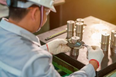 Üretim işçisi, mikrometre denetimi için yüksek metal ürünü kullanıyor.