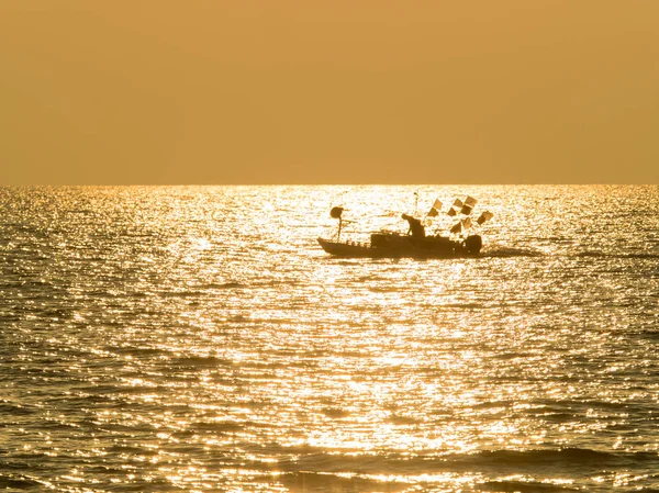 一个渔民的剪影在小渔船上的金色闪闪发光的大海在太阳 — 图库照片