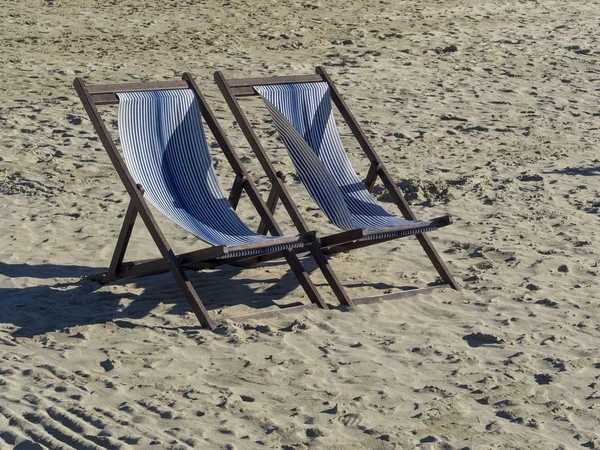 two wooden deck chair in white and blue stripes on a sandy beac