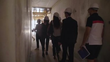 Bir grup işadamı ve kadın miğferli bir şantiyeyi ziyaret ediyor.