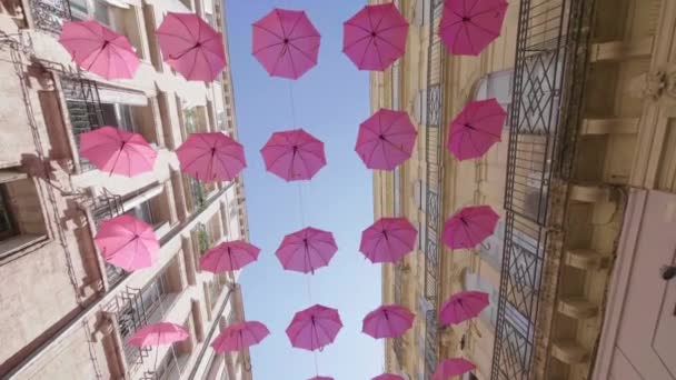 Pinkfarbene Regenschirme hängen zwischen zwei Gebäuden in Montpellier. Rosa Oktober — Stockvideo