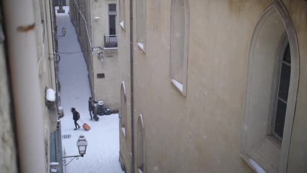 Άνθρωποι περπατούν σε χιονισμένους δρόμους με θέα τις βαλίτσες τους από ένα ψηλό παράθυρο. — Αρχείο Βίντεο