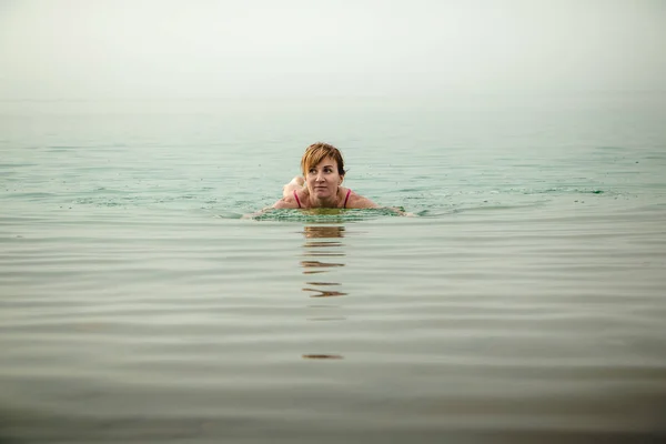 Funny girl swims in water of Dead Sea in Jordan and fog