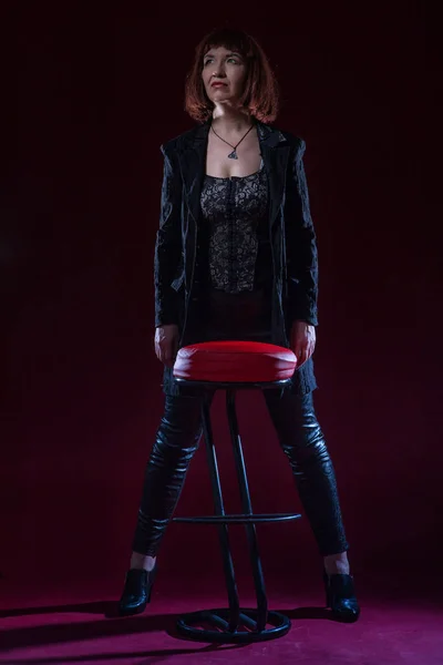 Confident ugly woman wearing black suit siting and posing in front of camera on stage with crimson floor