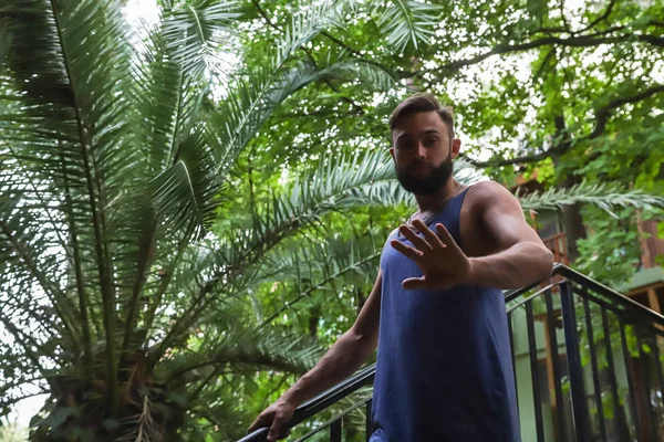 Young man with black hair and beard in the Park in a summer evening and green trees arround