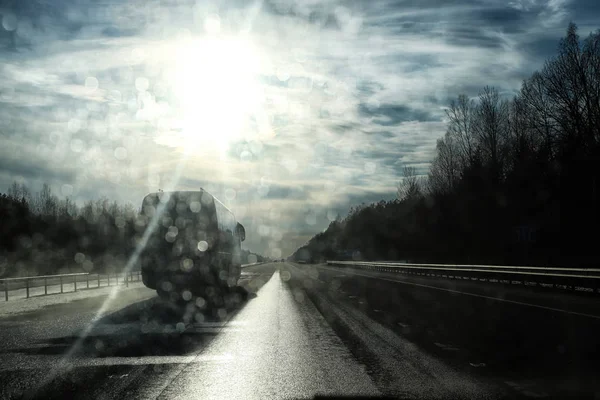 Road and glare from the sun on the car windshield in a spring evening. Illumination, overexposure and gray toning