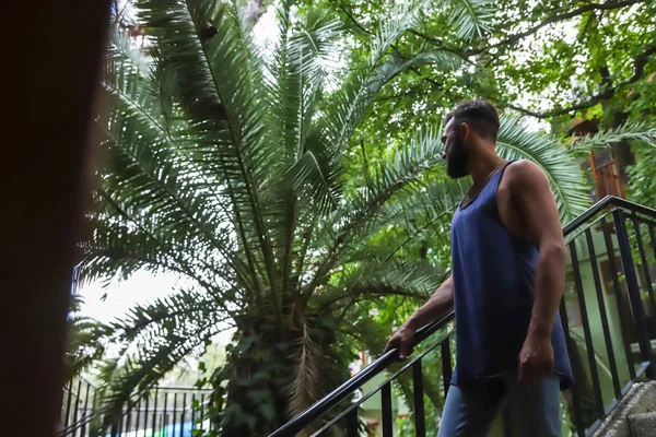 Young man with black hair and beard in the Park in a summer evening and green trees arround