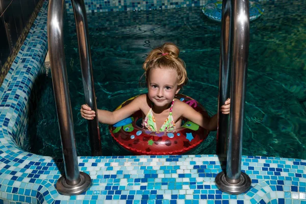 Nice child on the steps in blue small pool. Girl have fun in water indoors