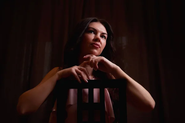 Mysterious portrait of a girl in a light dress in black room. Photo shoot in a dark key