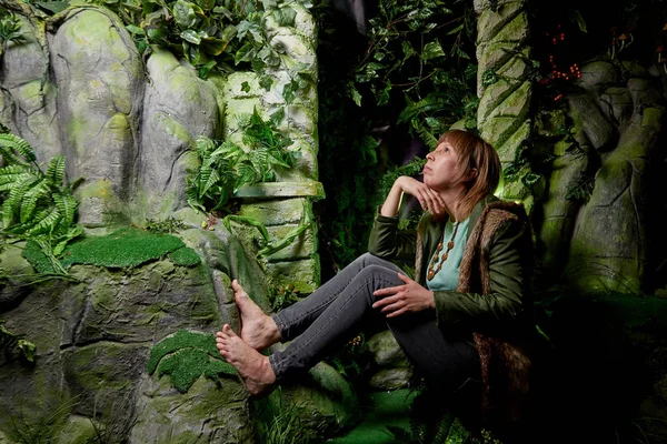 Girl in a green jacket with blond hair near an artificial rock with a grotto. Fabulous photo shoot in the Studio. Elf near his house. Dark key