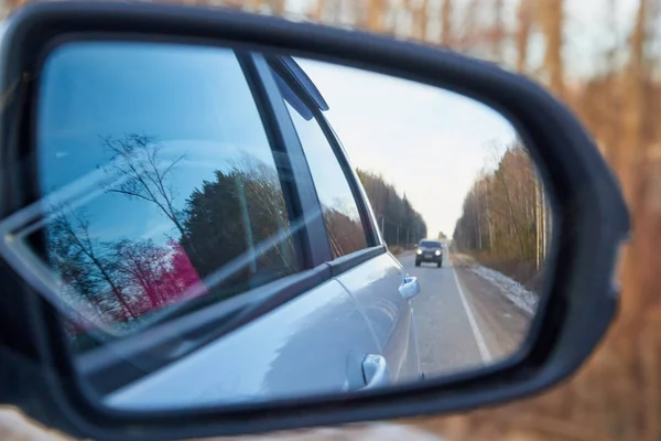 Side mirror of the car and the reflection of the road in it. Autumn landscape during travel. Looking through the mirror of a moving car