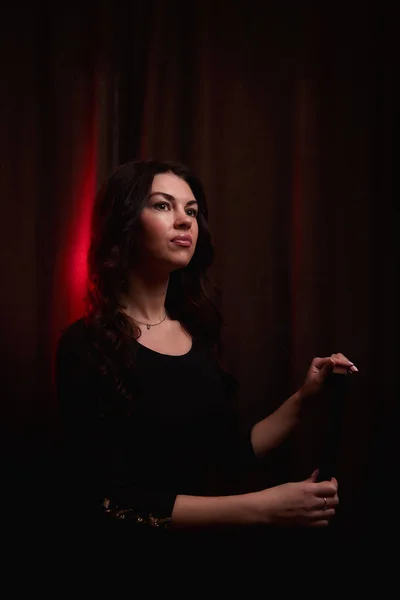 Mysterious portrait of a girl in black dress and red light background. Actress before going on stage. Photo shoot in a dark key