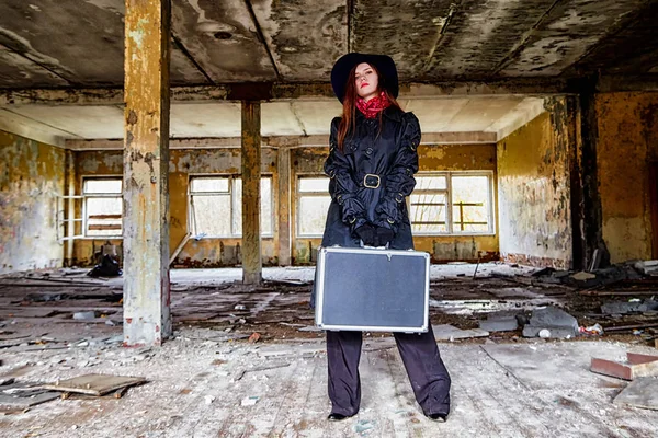 Girl in a black cloak and hat with a diplomat in a ruined room. A spy in a secret meeting. Unusual photo shoot