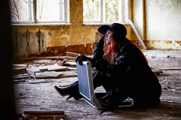 Girl in a black cloak and hat with a diplomat in a ruined room. A spy in a secret meeting. Unusual photo shoot