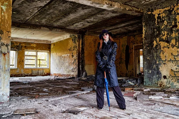 Girl in a black cloak and hat posing in an abandoned, ruined house. Unusual photo shoot