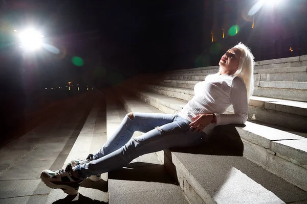 Ugly woman on the steps of stair in the city at night with lighting flashes in the black background