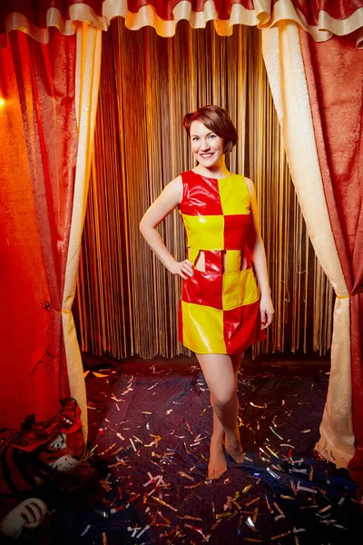 Young woman during a stylized theatrical circus photo shoot in beautiful red location. Models posing on stage with curtain