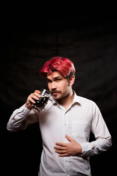 Young handsome guy with red hair in white shirt drinking beer and black background. Funny man with sad emotions on the face and a beer mug in hand. alcoholic with alcohol. Model in photoshoot